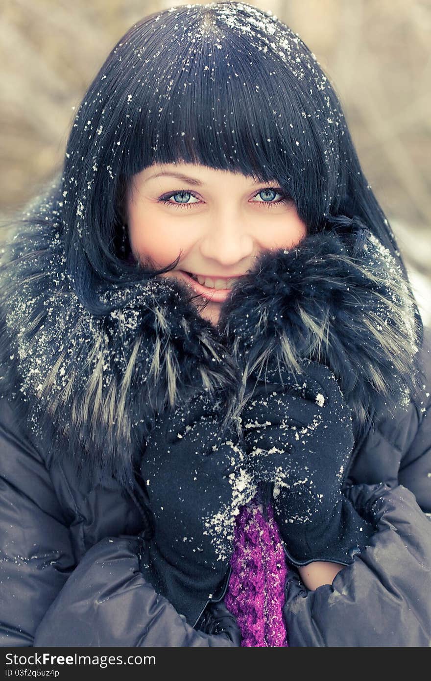 Attractive young woman in wintry coat with large fur head, snowy in background.