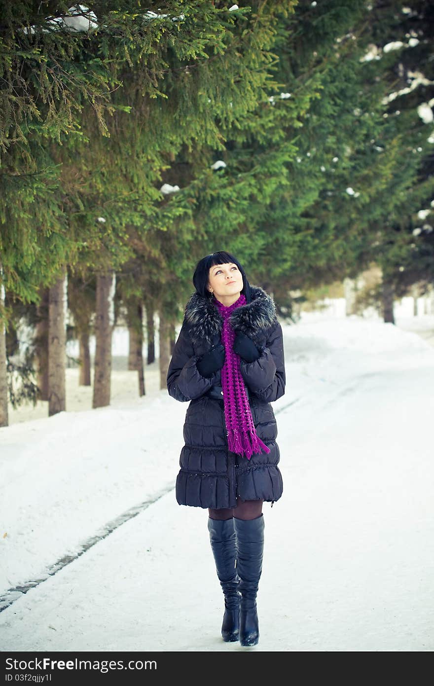 Attractive young woman in wintry coat with large fur head, snowy in background.