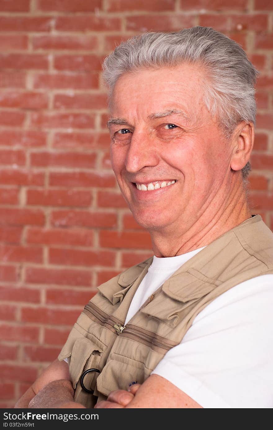 Old builder in the uniform on a brick background. Old builder in the uniform on a brick background