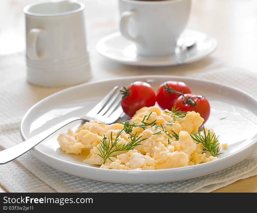 A plate of creamy scrambled eggs garnished with dill, a cup of coffe with milk. A plate of creamy scrambled eggs garnished with dill, a cup of coffe with milk