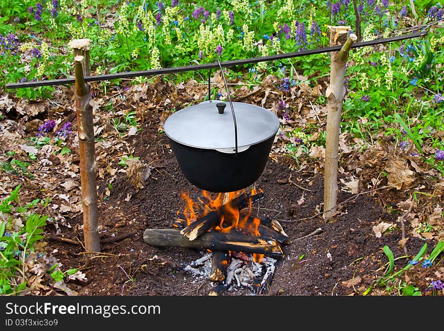 Outdoor summer. Cooks porridge in a pot on the fire. Outdoor summer. Cooks porridge in a pot on the fire