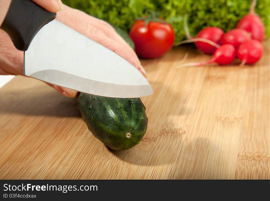 A lady is cutting a cucumber with a knife. A lady is cutting a cucumber with a knife