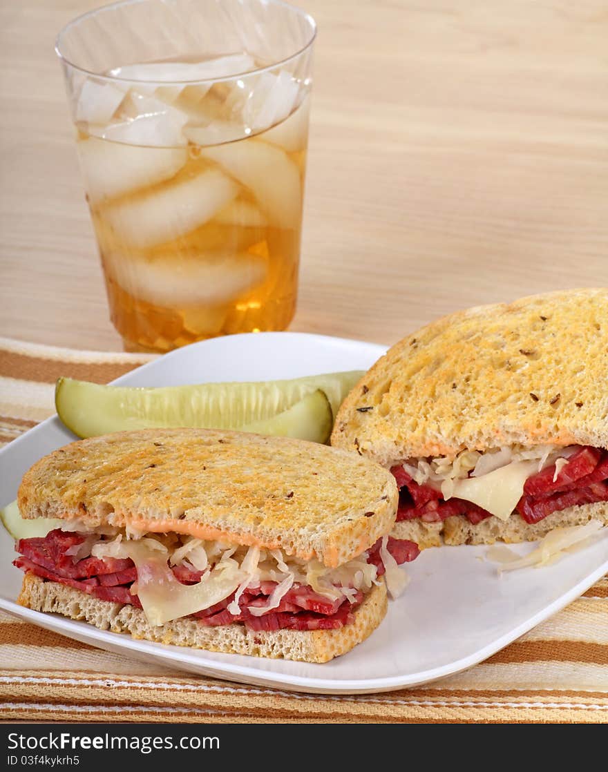 Corned beef sandwich with cheese and sauerkraut on rye bread, a pickle and drink