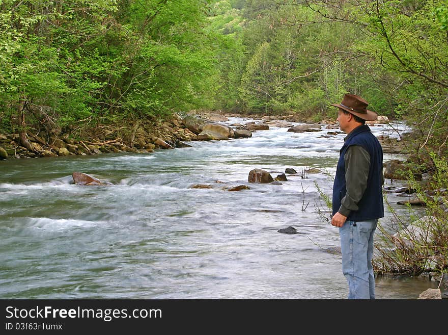 A hiker pauses by the bank of a creek. A hiker pauses by the bank of a creek