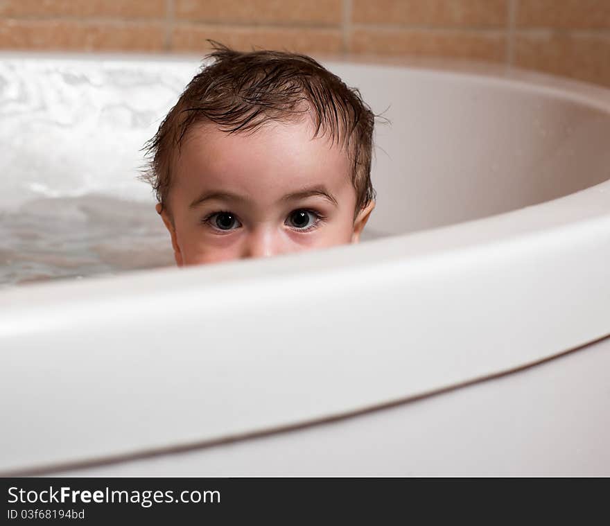 Little baby boy sits in bathtub, eyes