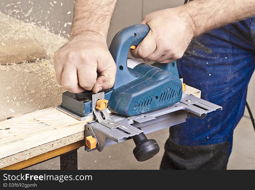 Close-up of a construction worker's hand and power tool while planing a piece of wood trim for a project. Close-up of a construction worker's hand and power tool while planing a piece of wood trim for a project.