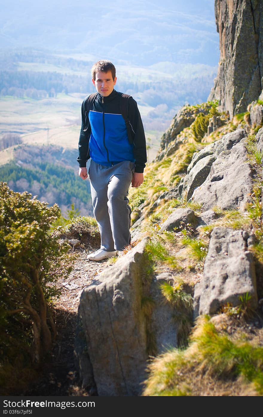 Man on a rocky wild path on high ground in the mountains with land down on the background. Man on a rocky wild path on high ground in the mountains with land down on the background.