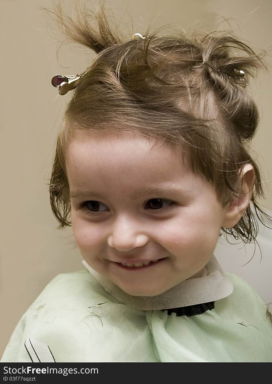 Small girl at hairdresser's, wearing hairpins and a cape, smiling