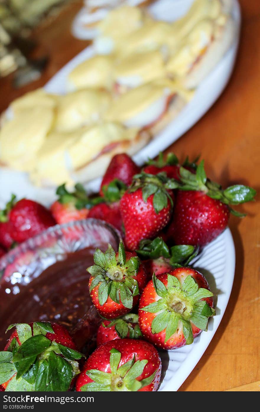 Some ripe strawberries sit around a bowl of chocolate dip with oter desserts in the background. Some ripe strawberries sit around a bowl of chocolate dip with oter desserts in the background.