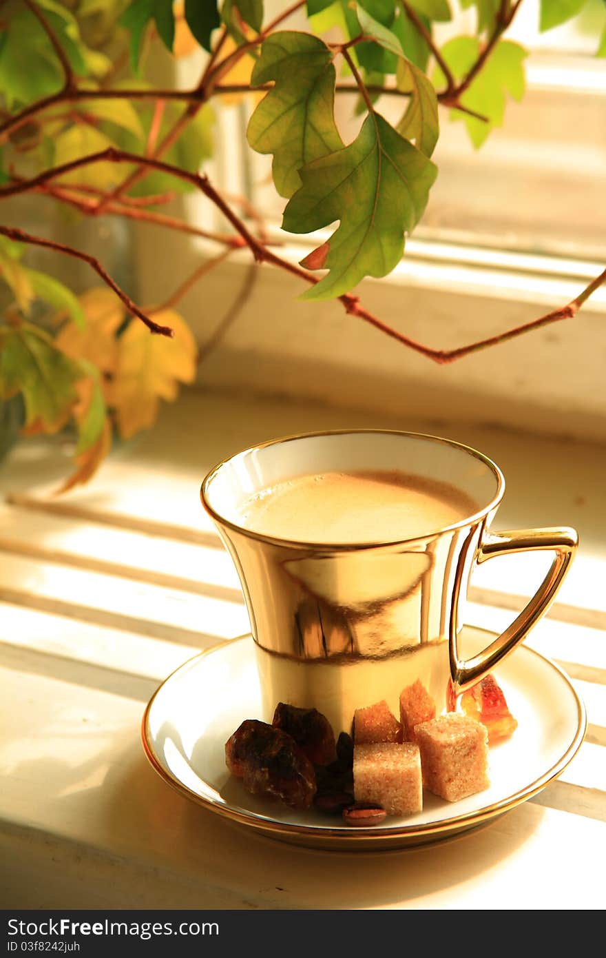 Coffee in gold cup with brown sugar and blured leaves on background