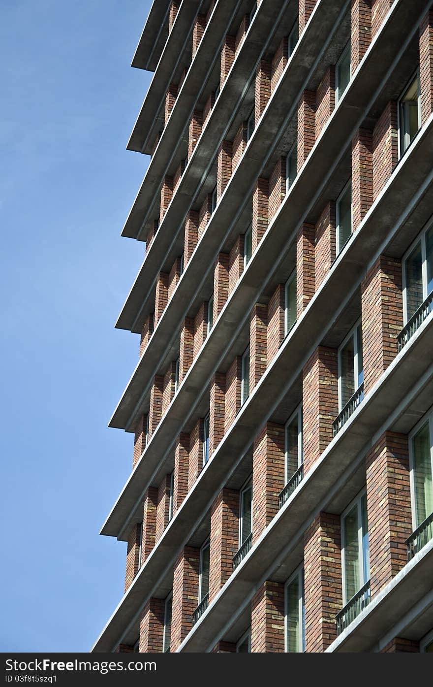 Fragment of the facade of the modern brick residential house with the same balcony. Detail. Against the blue sky.