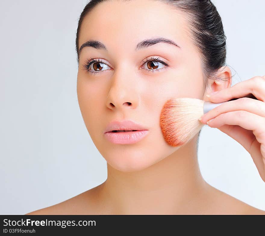 Beautiful woman applying make-up with brush