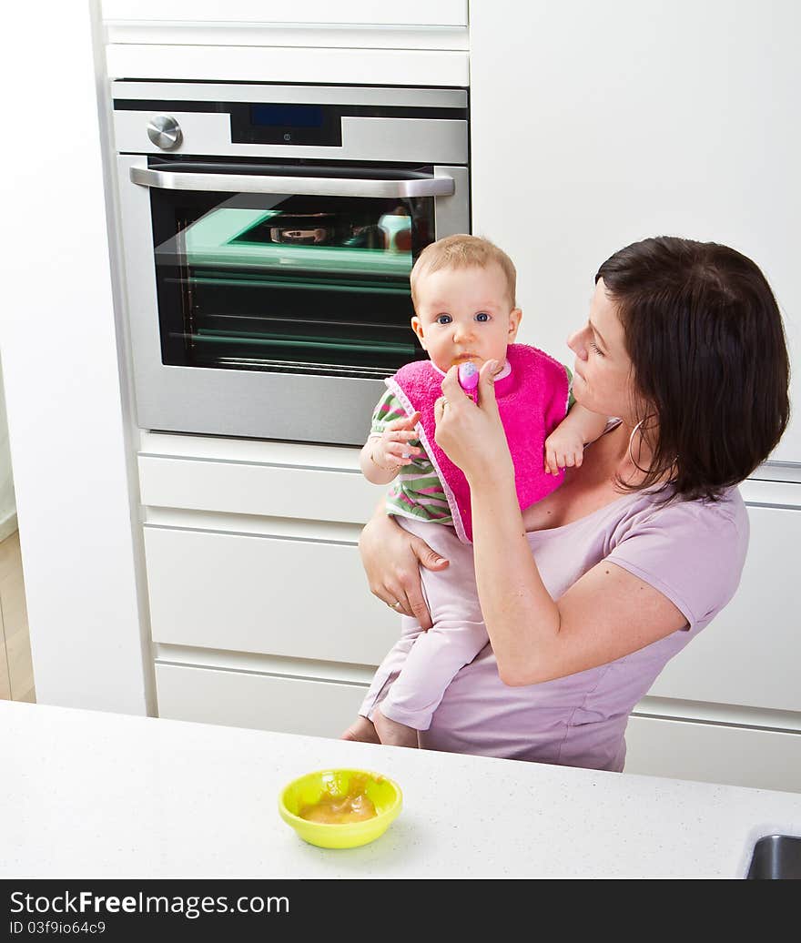 Young mother is feeding her baby in a modern kitchen setting. Young mother is feeding her baby in a modern kitchen setting.