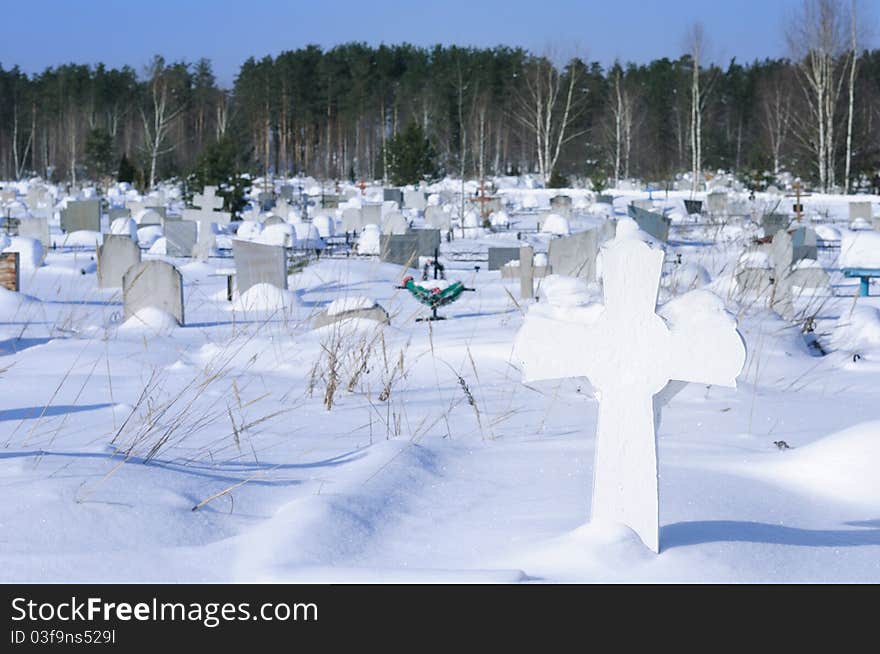 View of the snow-covered cemetery with a cross in the foreground. View of the snow-covered cemetery with a cross in the foreground