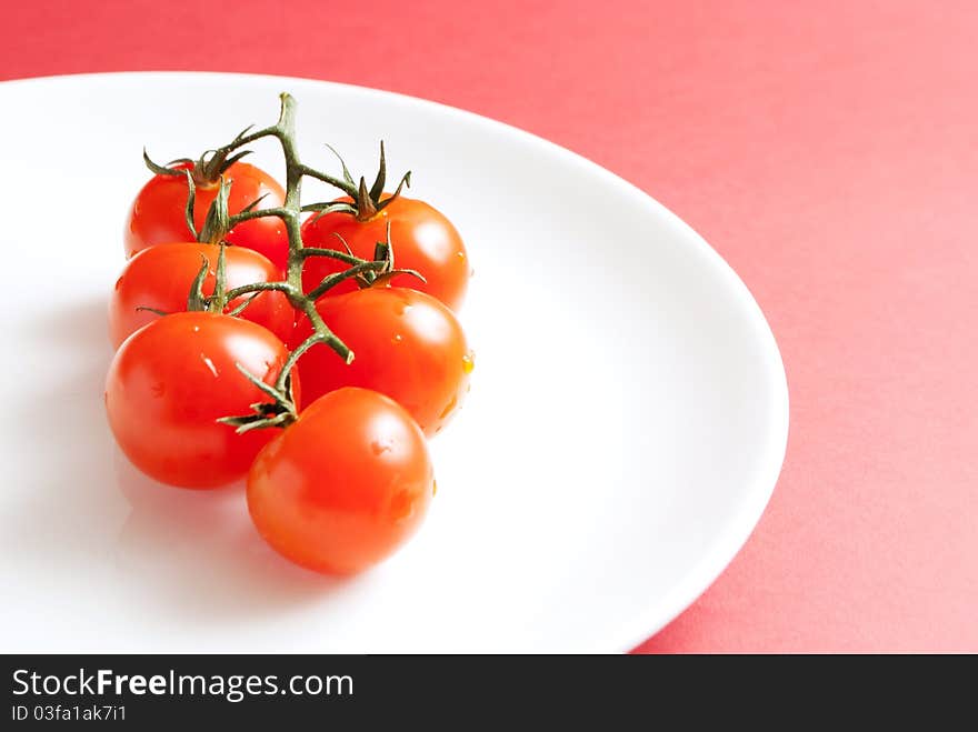 Stem of cherry tomatoes on white pkate and red underground