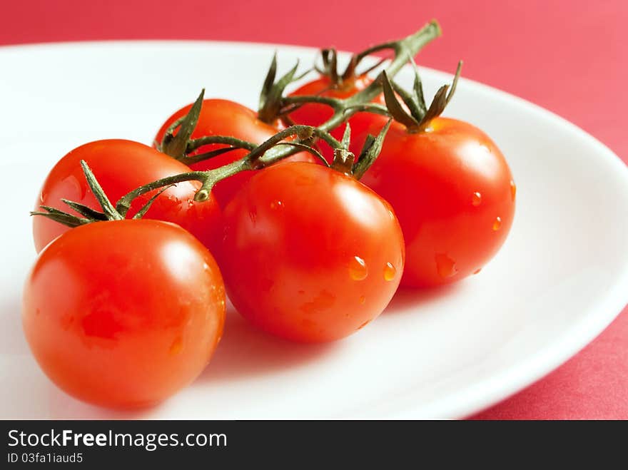 Closeup of cherry tomatoes stem on white plate and red background. Closeup of cherry tomatoes stem on white plate and red background