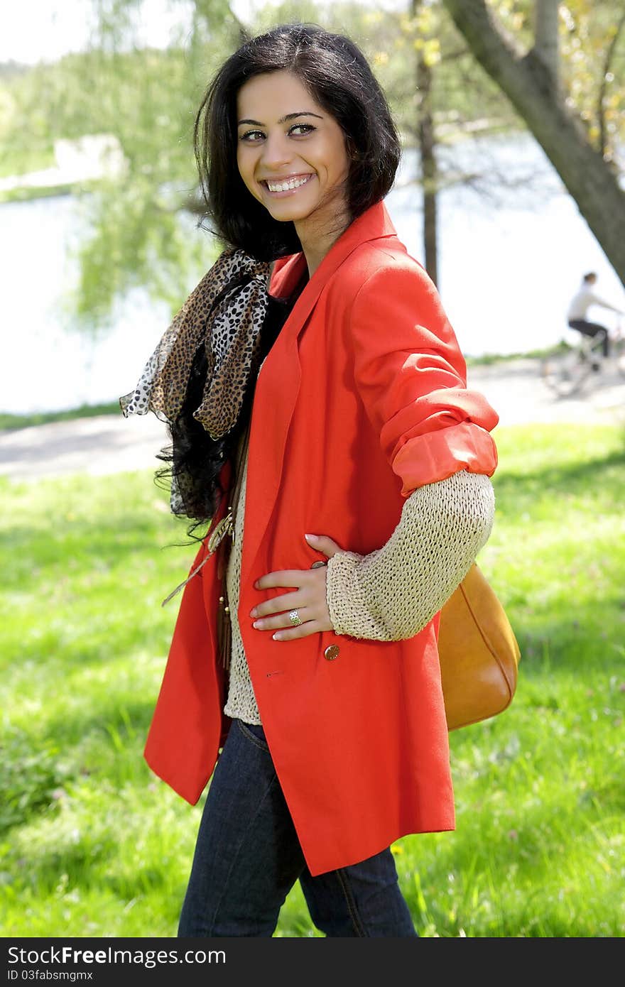 Beautiful brunette girl in red coat at the park