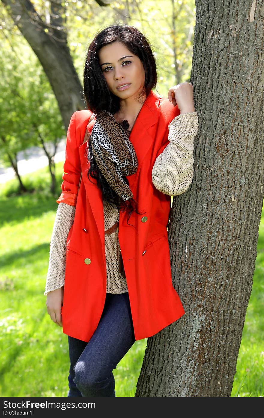 Beautiful brunette girl in red coat at the park