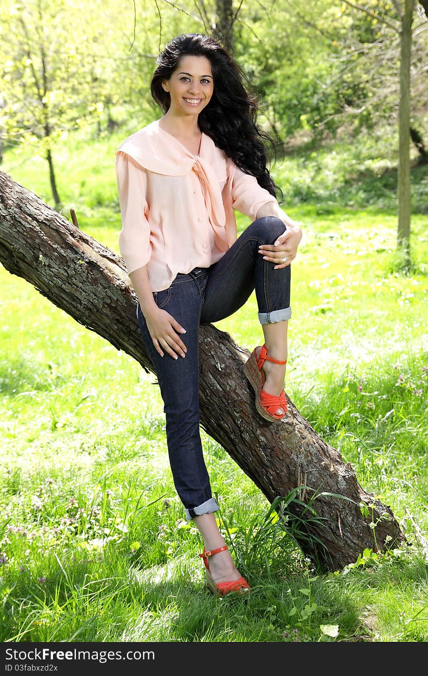 Beautiful young brunette model sitting on a tree in park. Beautiful young brunette model sitting on a tree in park