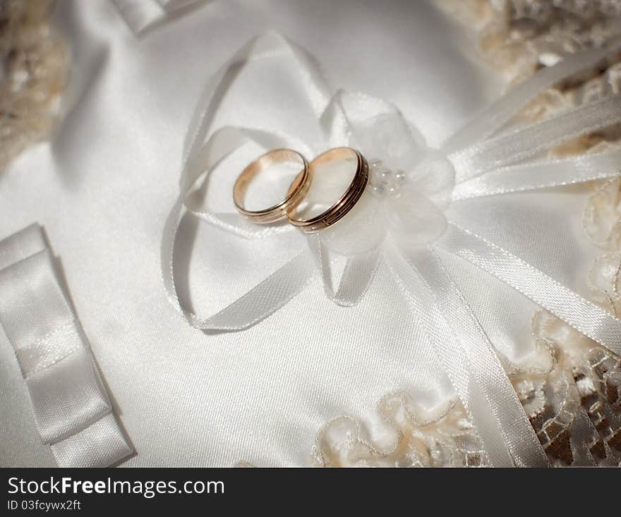 Pair of gold wedding rings on a white wedding pillow