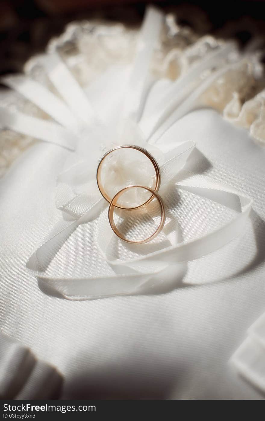 Pair of gold wedding rings on a white wedding pillow