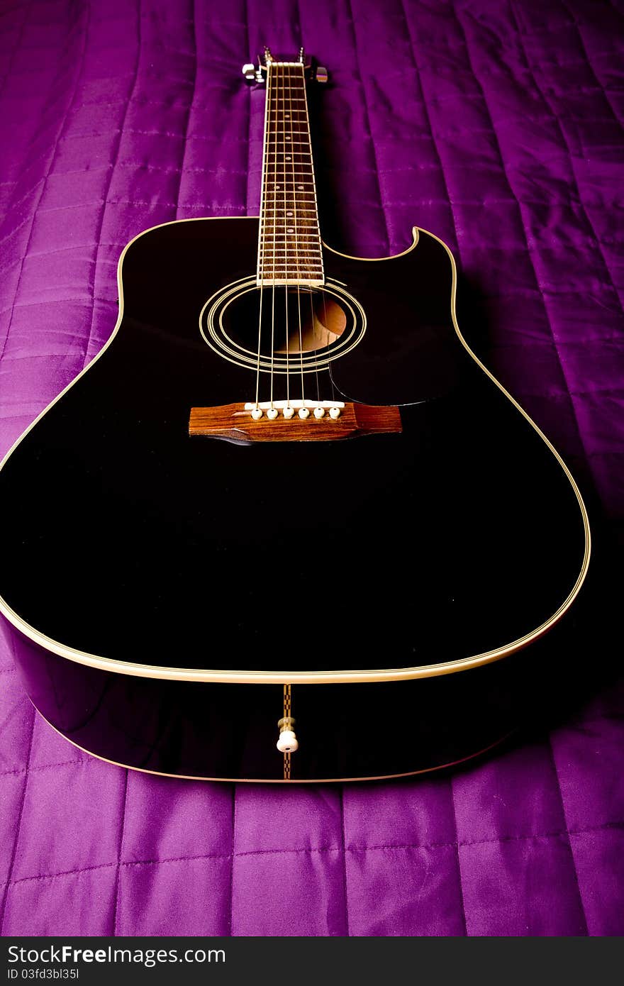 Black shiny acoustic guitar on bed. Black shiny acoustic guitar on bed