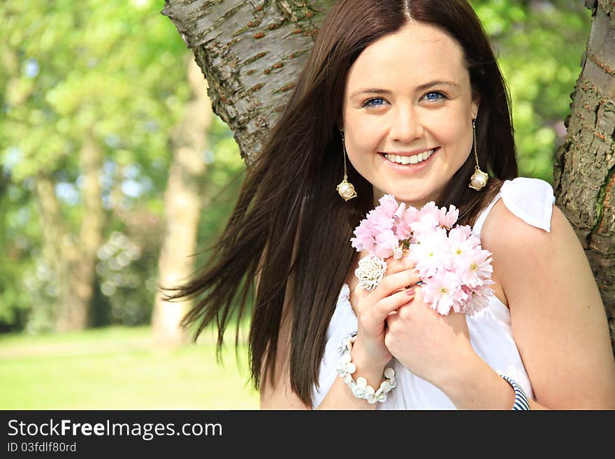 A happy woman holds and small bunch of flower close to her as she is enjoying a summers day.