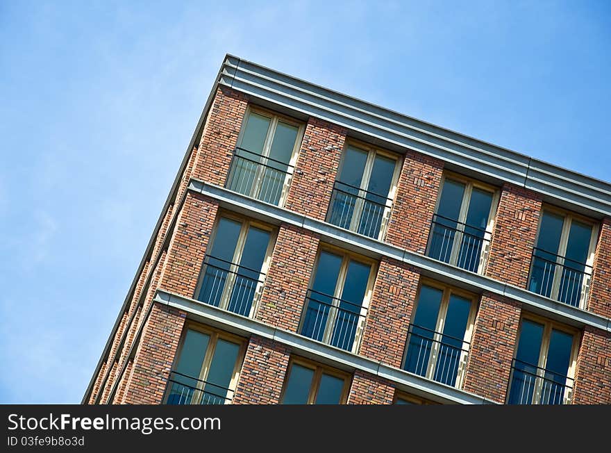 Fragment of the facade of the modern brick residential house with the same balcony. Detail. Against the blue sky.