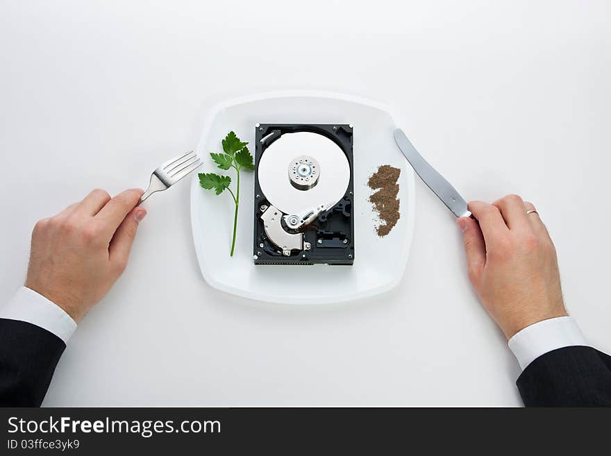 Hard drive is on the dining plate with seasoning and herbs. Men's hands hold a knife and fork. Hard drive is on the dining plate with seasoning and herbs. Men's hands hold a knife and fork