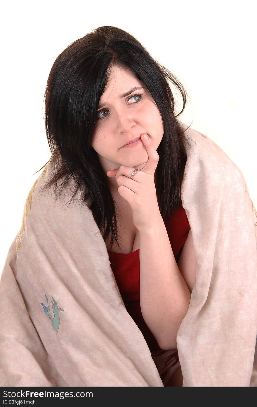 A young girl sitting on the floor covert in a blanket holding her finger to her mouths and thinking hard, for white background. A young girl sitting on the floor covert in a blanket holding her finger to her mouths and thinking hard, for white background.