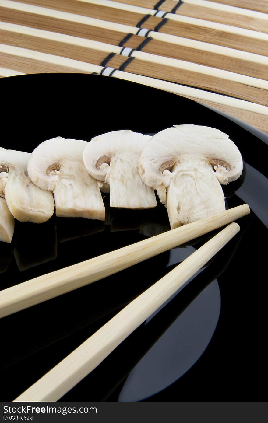 Mushrooms and chopsticks on black plate. Mushrooms and chopsticks on black plate