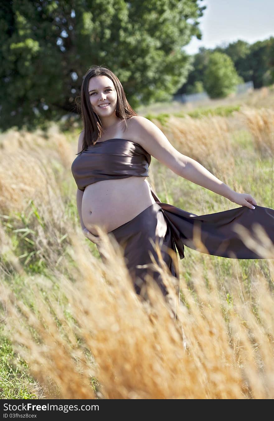 Pregnant woman wrapped in silk fabric outdoors in a field.