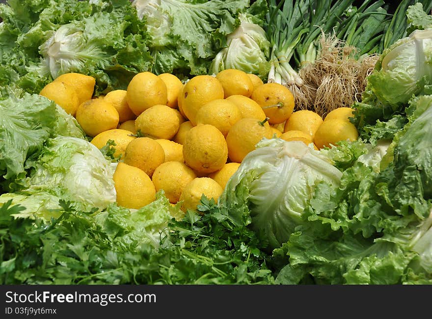 Fresh, moist yellow lemons surrounded by green salad ingredients lettuces, parsley, and green onions with roots all healthy low glycemic index foods. Fresh, moist yellow lemons surrounded by green salad ingredients lettuces, parsley, and green onions with roots all healthy low glycemic index foods.