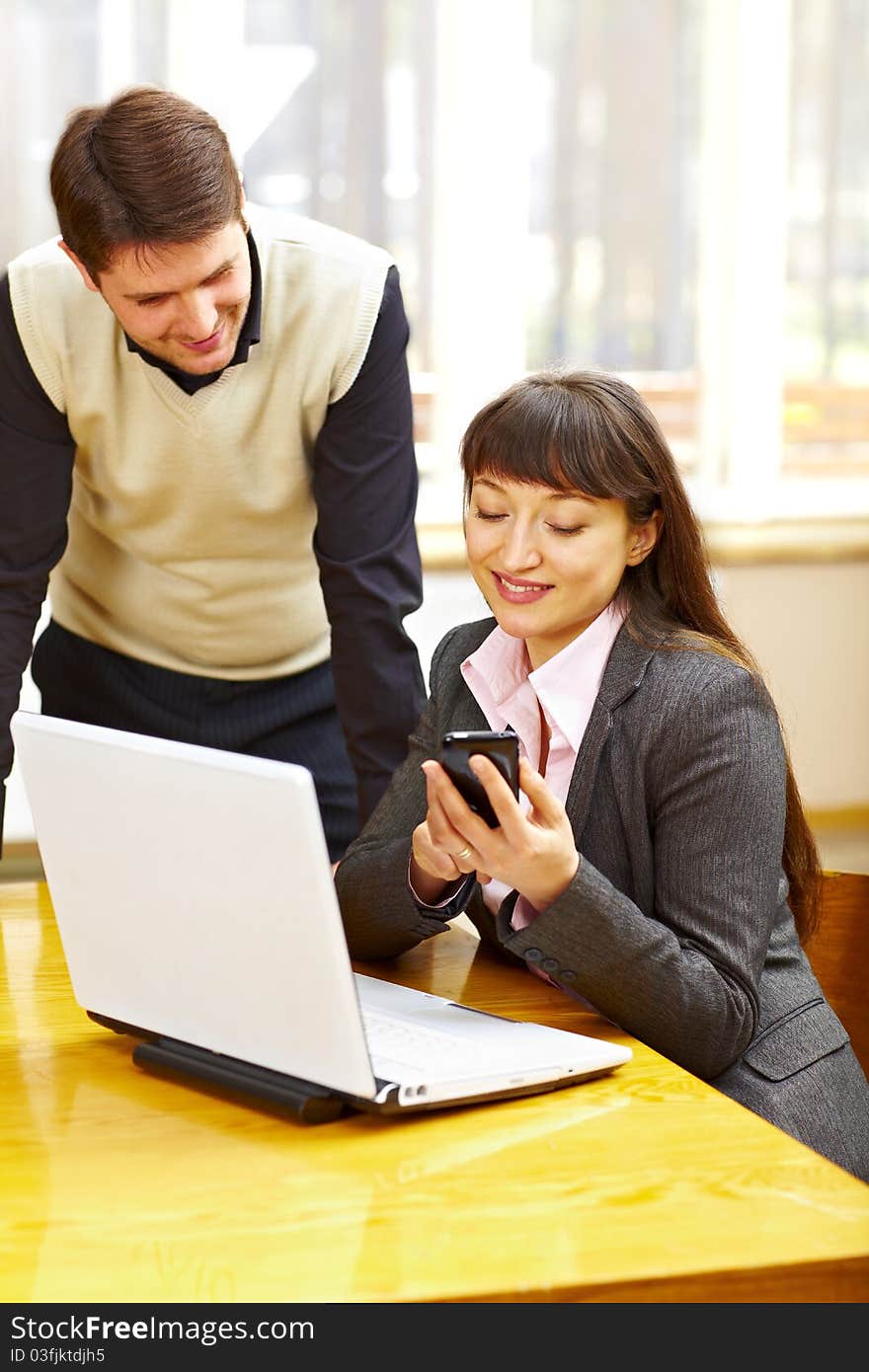 Business woman sitting at the table with laptop and showing something to her collegue on phone. Business woman sitting at the table with laptop and showing something to her collegue on phone