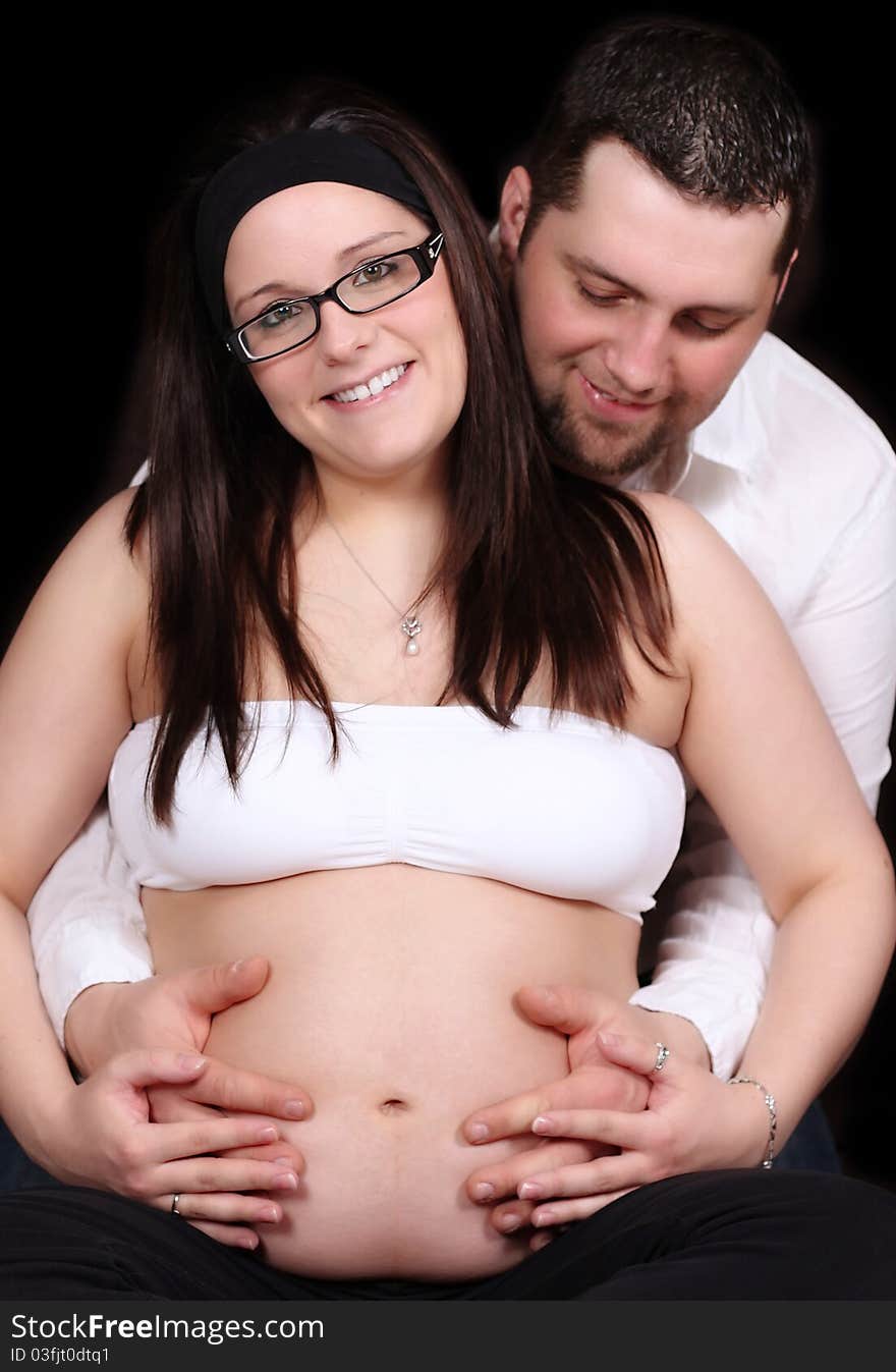 Happy expectng couple sitting with hands on her bare belly. Happy expectng couple sitting with hands on her bare belly