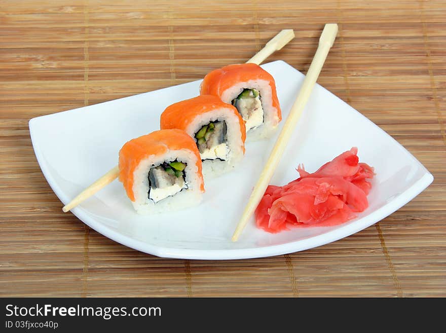 Close up of the three rolled salmon with conger, cucumber and ginger and two chopsticks on the white plate on the bamboo napkin background. Close up of the three rolled salmon with conger, cucumber and ginger and two chopsticks on the white plate on the bamboo napkin background.