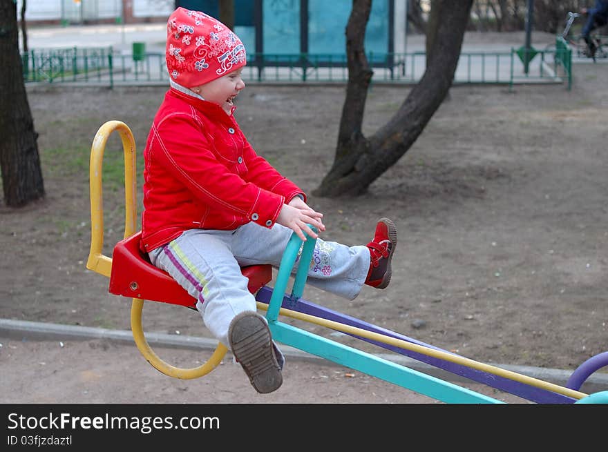 Pretty little girl play on the playground seesaw (teeter-totter). Pretty little girl play on the playground seesaw (teeter-totter).