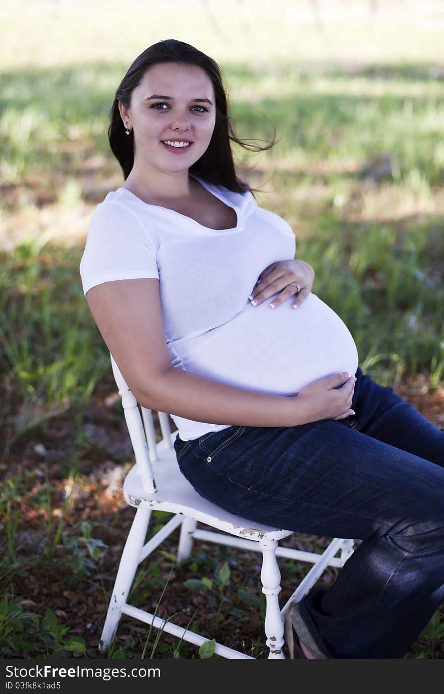 Pregnant woman sitting outside wearing jeans and t-shirt.