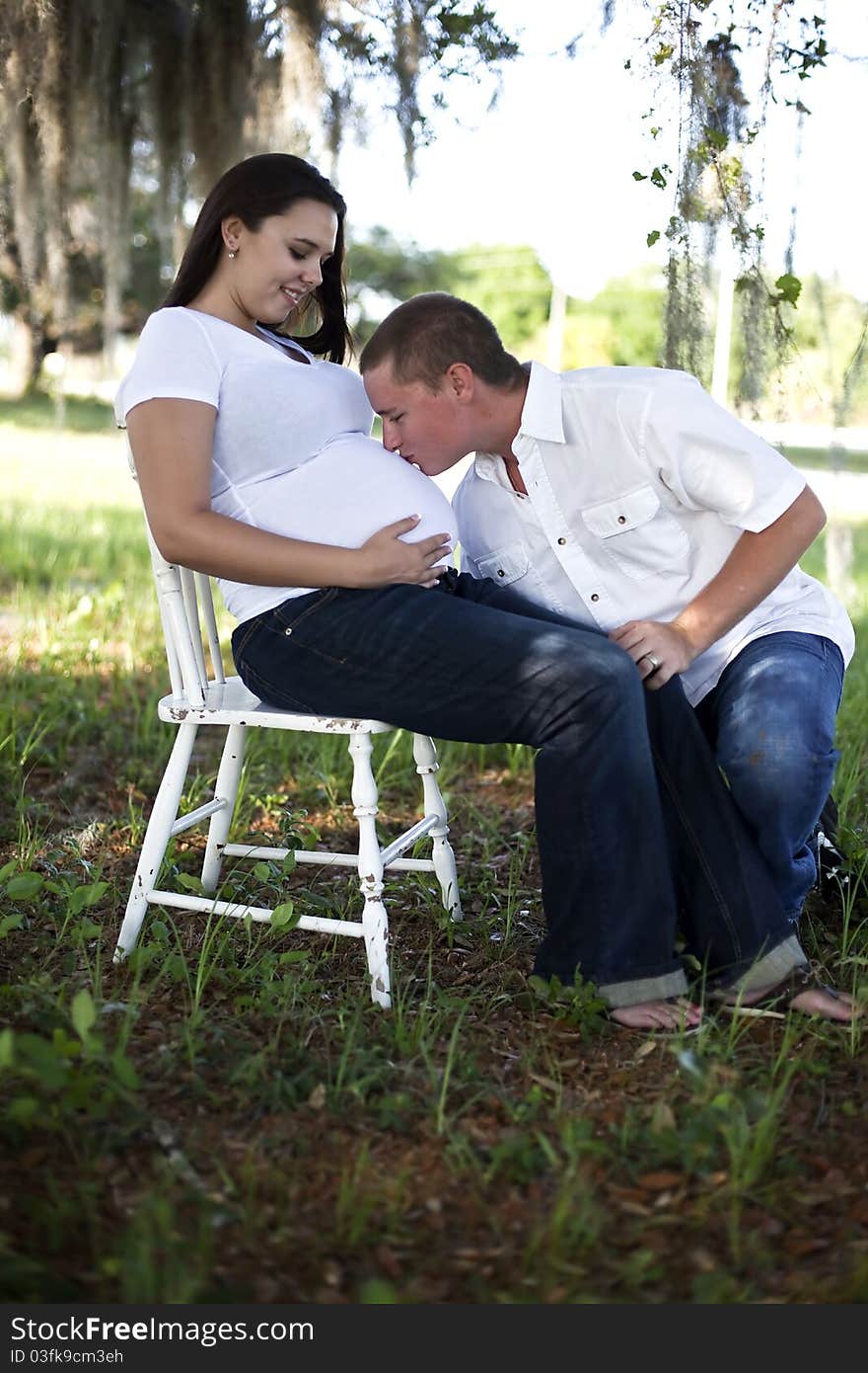 A young man kissing the belly of a pregnant young woman outdoors. A young man kissing the belly of a pregnant young woman outdoors.