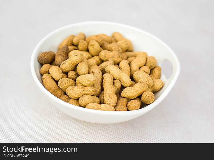 Pile of ripe crude peanuts in white bowl