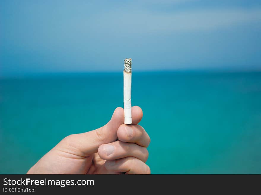 Hand holds a cigarette in the background of the sea