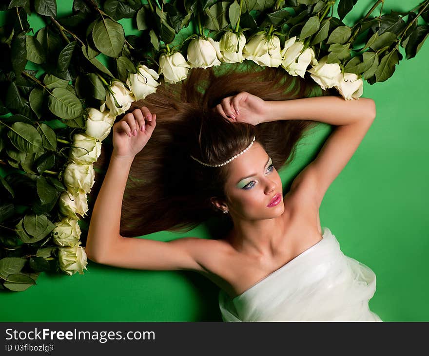 Young girl lay among the flowers of roses on a green background