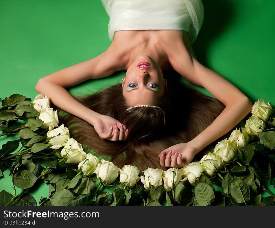 Young girl lay among the flowers of roses on a green background