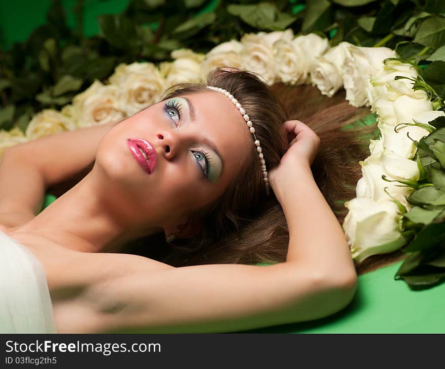 Young girl lay among the flowers of roses on a green background