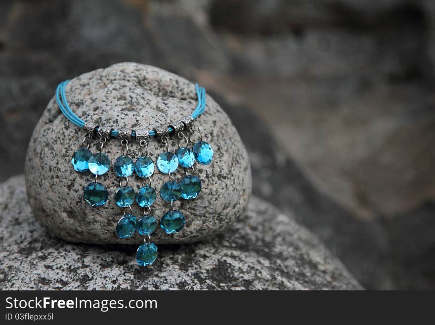 Blue gem necklace on a round grey rock. Blue gem necklace on a round grey rock