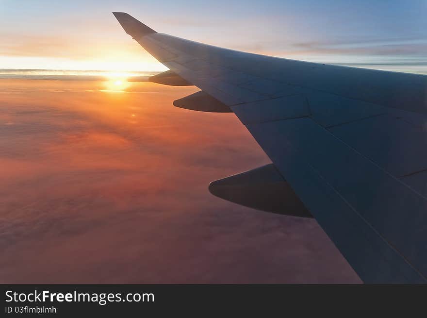 Airplane left wing on sunrise with a cloudy orange sky. Airplane left wing on sunrise with a cloudy orange sky