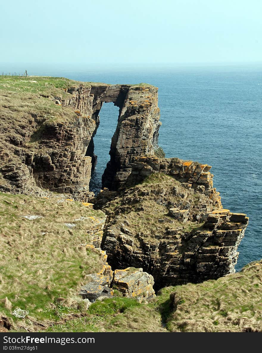 A Coastal Arch, near Wick. Caithness, Scotland, UK. The Arch is on the North east Coast of Scotland. This coastal arch called the Brig O Trams lies 5.6km south of Wick, Caithness, far North East Scotland, UK, Europe. The North sea has eroded and shaped this part of the cliff into a natural arch and bridge. The roof will collapse in time to form a free-standing stone stack. Caithness and North Coast Sutherland is a large area of unspoilt, dramatic scenery in the far north of Scotland, indeed, on the extreme edge of Europe. The borders of Caithness are the Pentland Firth to the north and Moray Firth to the east.