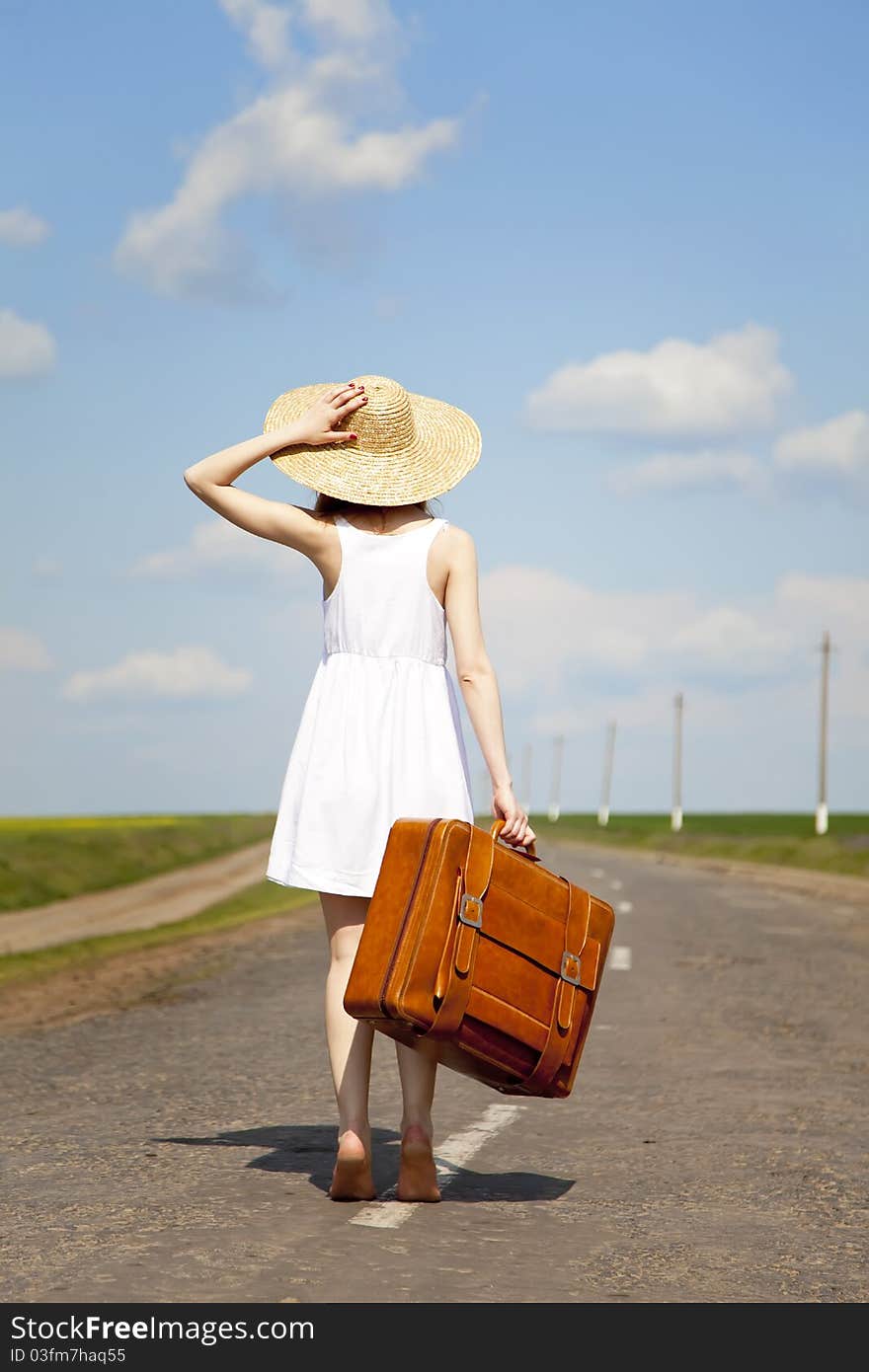 Lonely girl with suitcase at country road.