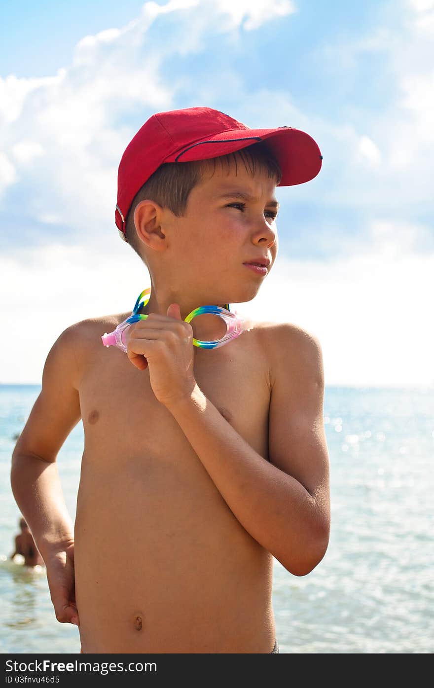 A boy in a baseball cap, standingagainst the backdrop of the sea