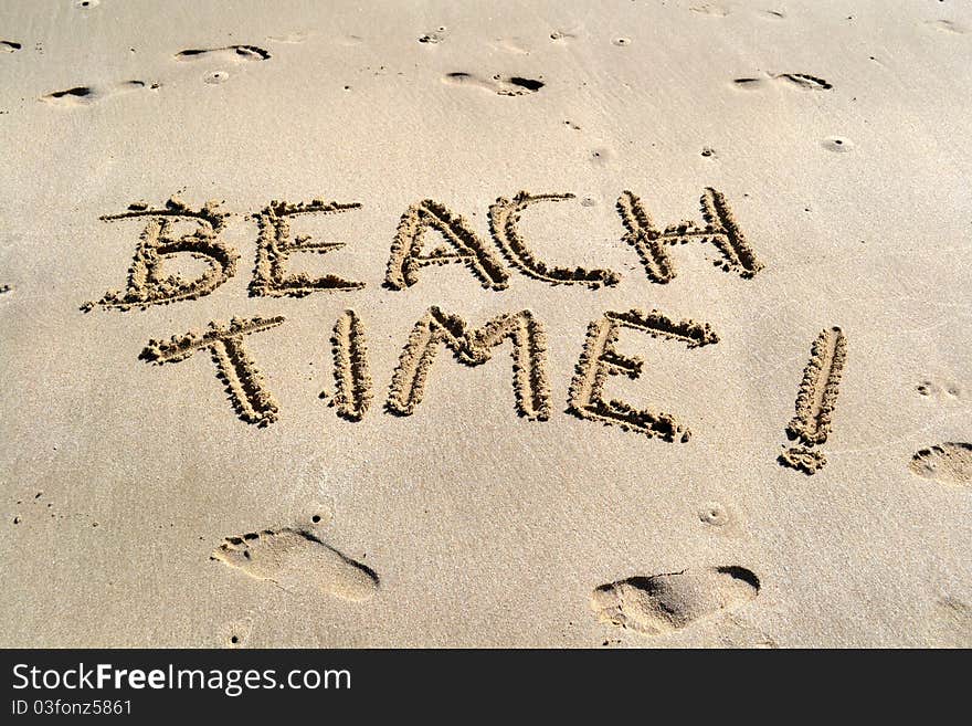 Beach Time carved in the sand with barefoot prints around it. Beach Time carved in the sand with barefoot prints around it.